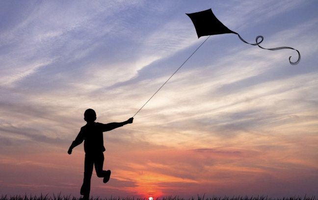 Silhouette of a person flying a kite at sunset.